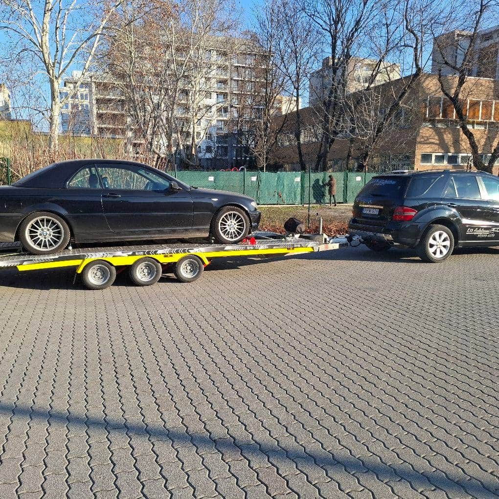 Fekete személyautó tréleren, a K13 Autotrans fekete Mercedes terepjárójával vontatva