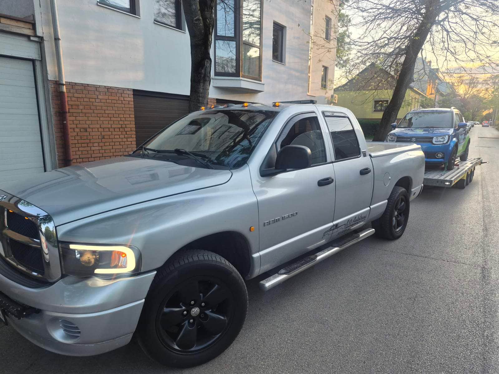 Kék autó szállítása tréleren lakóutcában az ezüst Dodge Ram pickuppal