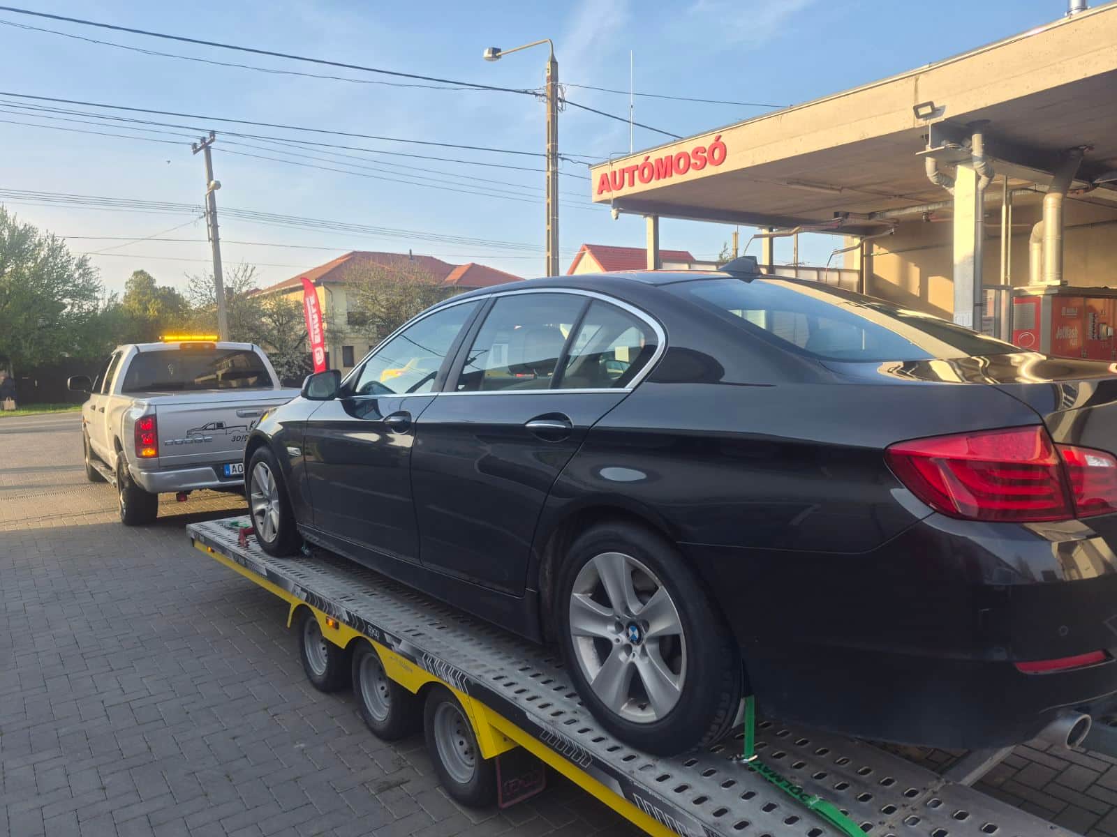 Fekete BMW 5-ös tréleren egy autómosónál, sárga villogós vontatóval
