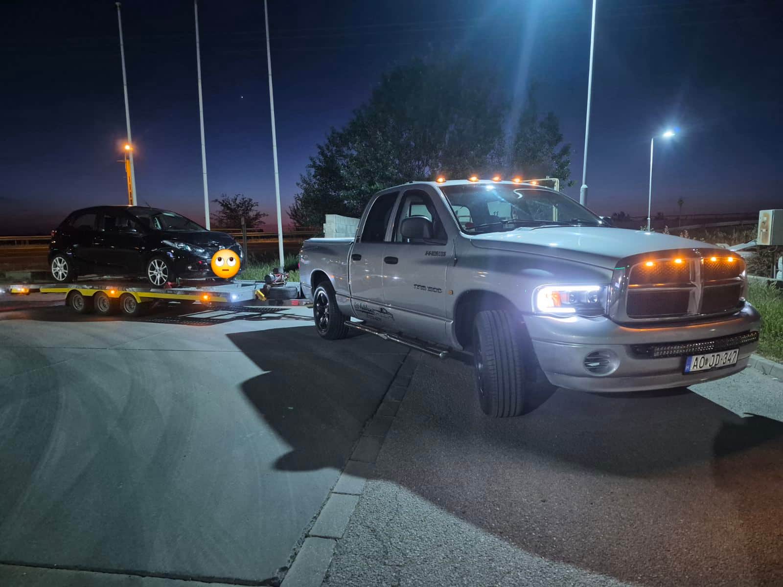 Éjszakai autómentés: ezüst Dodge Ram pickup, mögötte tréleren egy fekete autó