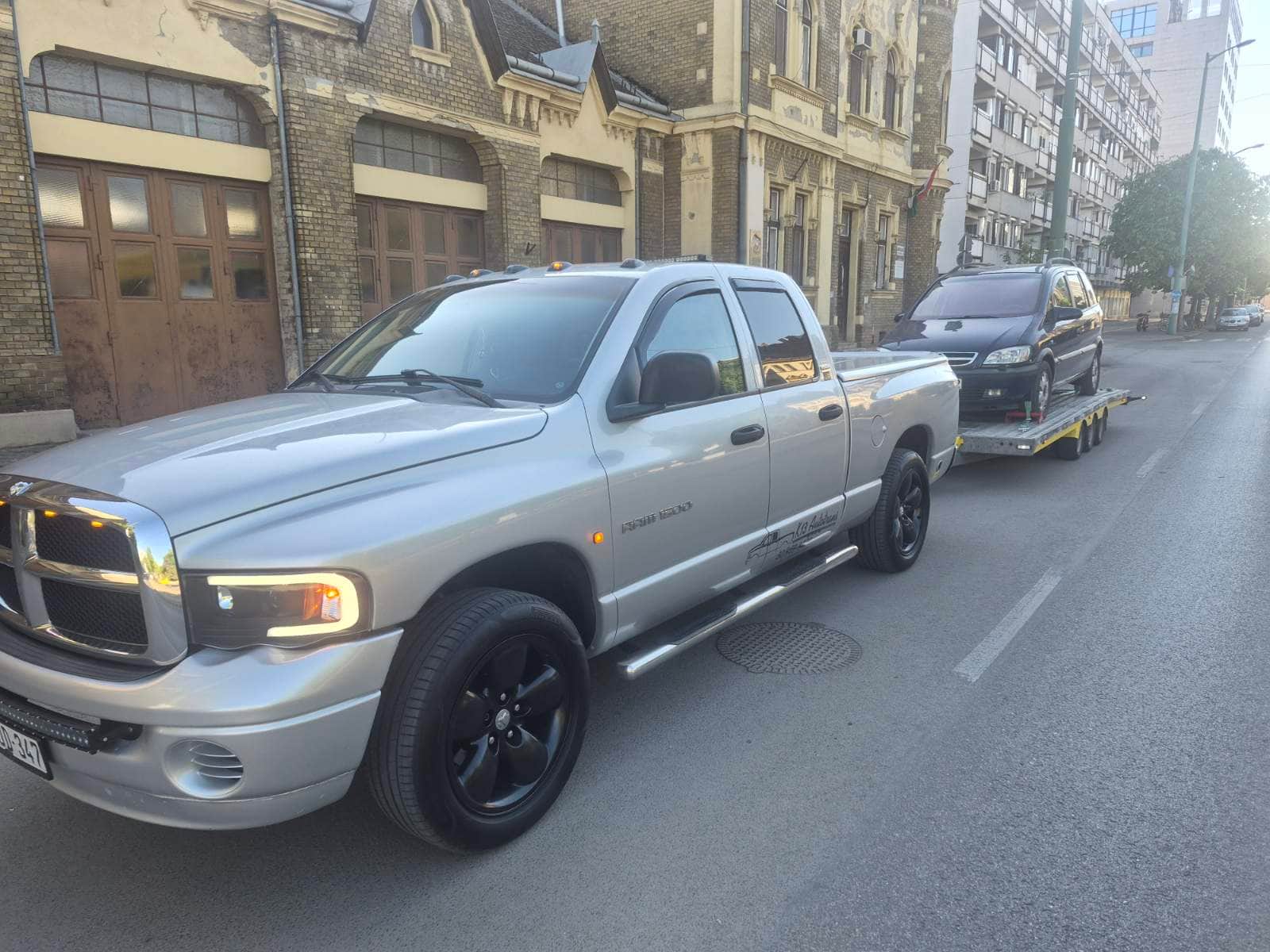 Autószállítás városi utcán az ezüst Dodge Ram vontatóval